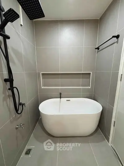 Modern bathroom with sleek bathtub and rainfall showerhead in elegant gray tiles.
