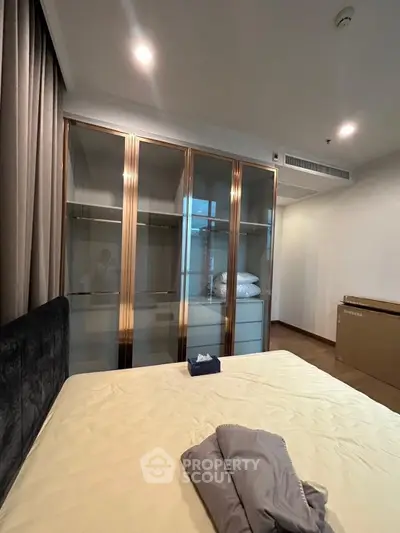 Luxurious bedroom with elegant glass wardrobe and cozy bedding in modern apartment.