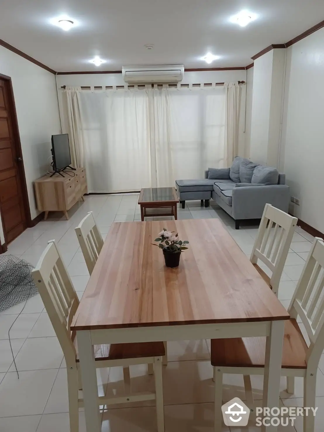 Spacious and well-lit living room with large dining table, comfortable seating area, and modern air conditioning unit, perfect for family gatherings.