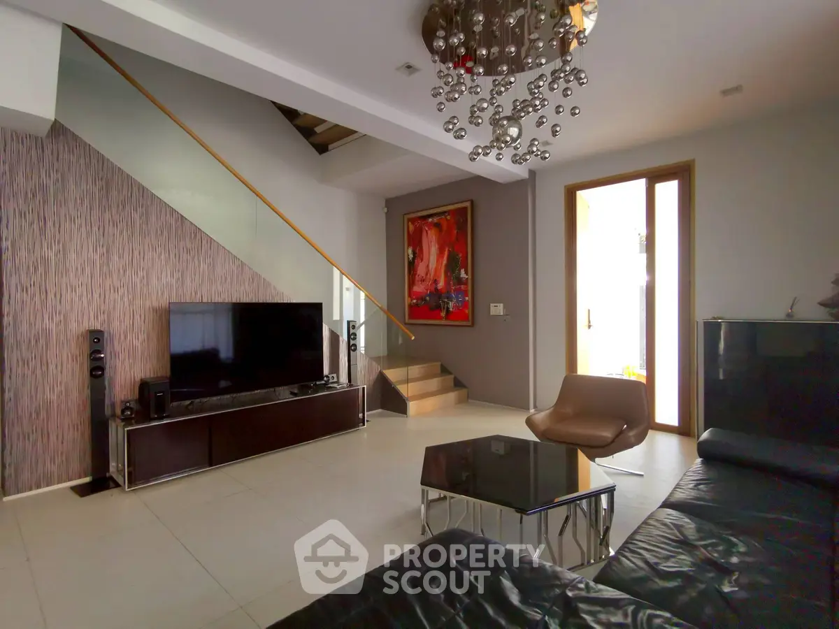 Modern living room with stylish decor and staircase, featuring a sleek TV setup and contemporary furniture.