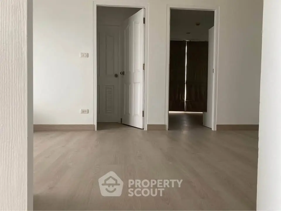 Spacious empty room with light wood flooring and white doors, perfect for customization.