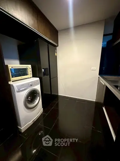 Modern kitchen with sleek black flooring and appliances, featuring a washing machine and oven.