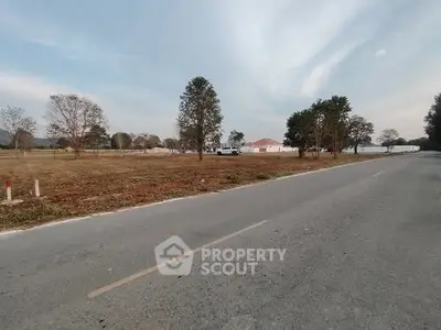 Expansive land plot with road access and distant view of a house, ideal for development.