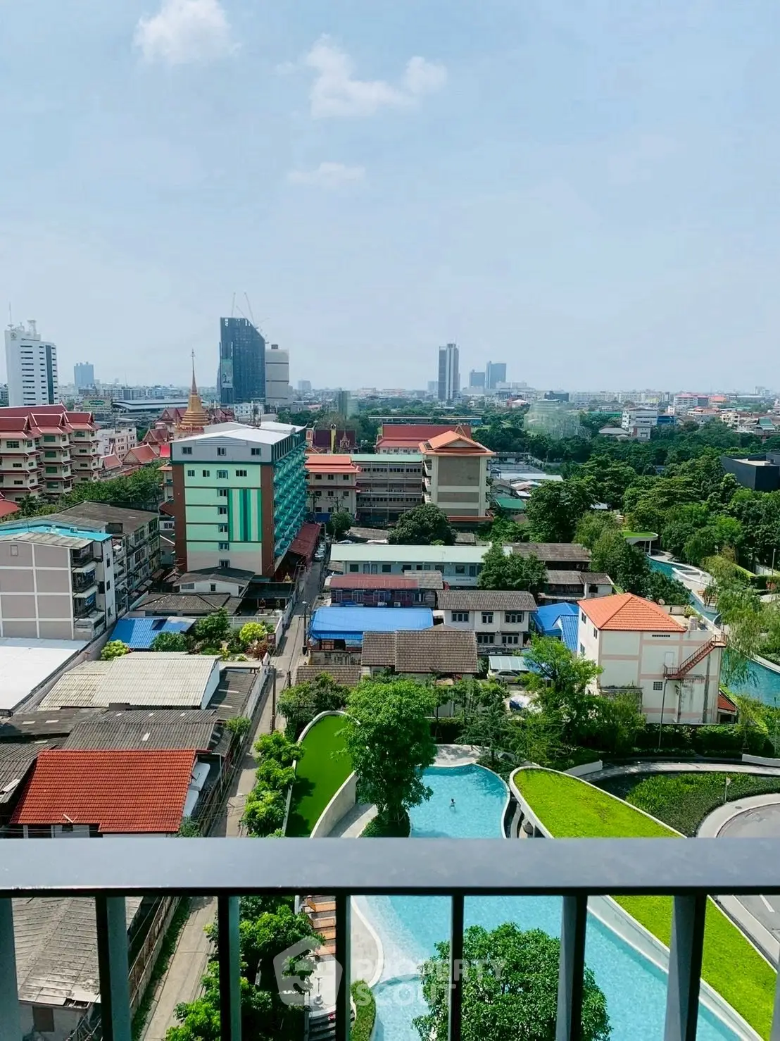 Stunning cityscape view from high-rise balcony with lush greenery and pool below.