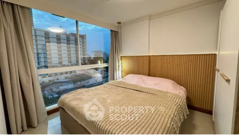 Cozy bedroom with large window offering city view, featuring modern decor and soft lighting.