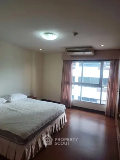 Spacious bedroom with large window and wooden flooring in modern apartment.