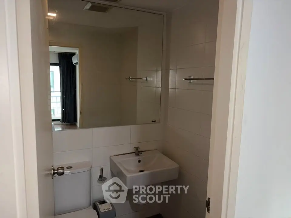 Modern bathroom with sleek fixtures and a large mirror, offering a glimpse into a bright adjoining room.