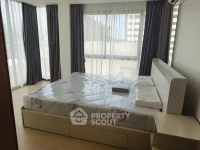 Spacious bedroom with large windows and modern furnishings in a high-rise apartment.