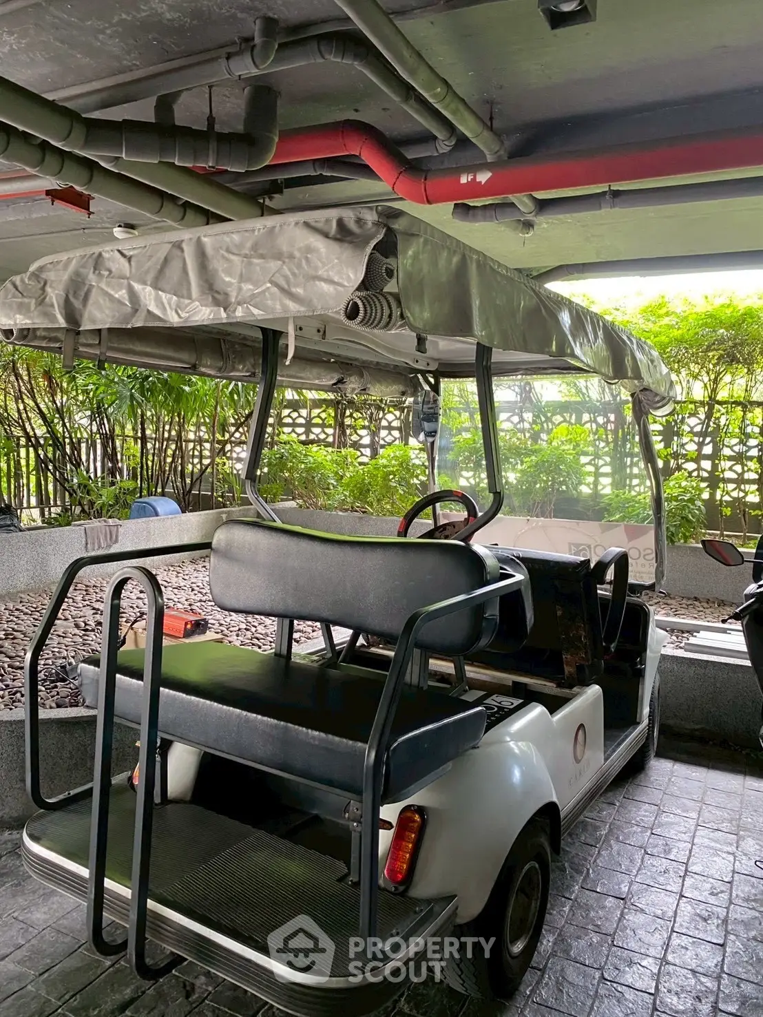 Covered golf cart parked in a residential parking area with greenery in the background.