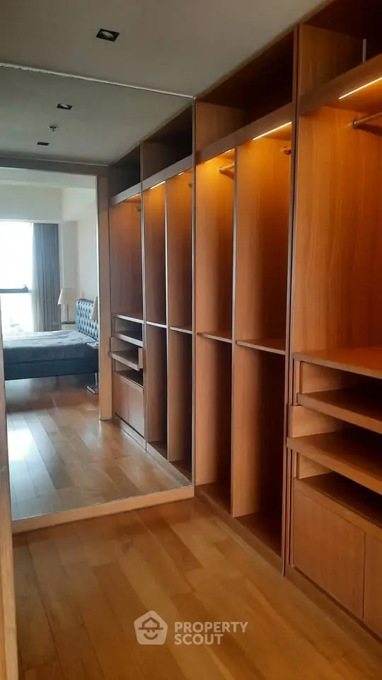 Luxurious walk-in closet with wooden shelves and mirror, leading to a stylish bedroom with natural light.