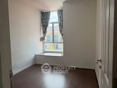 Cozy bedroom with large window and wooden flooring, perfect for natural light lovers.