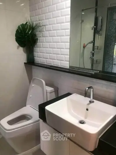 Modern bathroom with sleek sink and toilet, featuring stylish white brick tiles and a decorative plant.