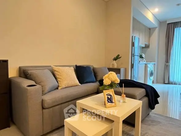Modern living room with cozy sofa and open kitchen layout featuring washing machine.