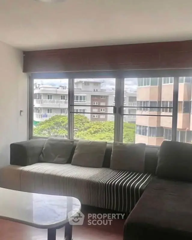 Spacious living room with large windows offering a city view, featuring a modern sectional sofa.