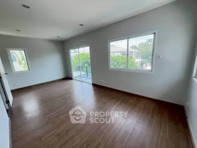Spacious empty room with wooden flooring and large windows offering natural light and a view.
