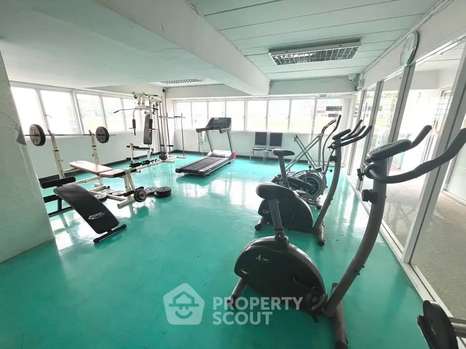 Spacious gym with modern fitness equipment and large windows for natural light.