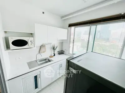 Modern kitchen with sleek white cabinets and large window offering city views.