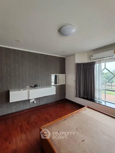 Spacious bedroom with wooden flooring and large window offering natural light