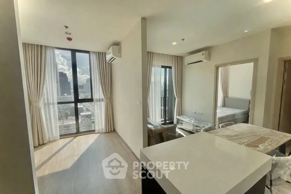 Modern apartment interior with open layout and city view, featuring large windows and natural light.