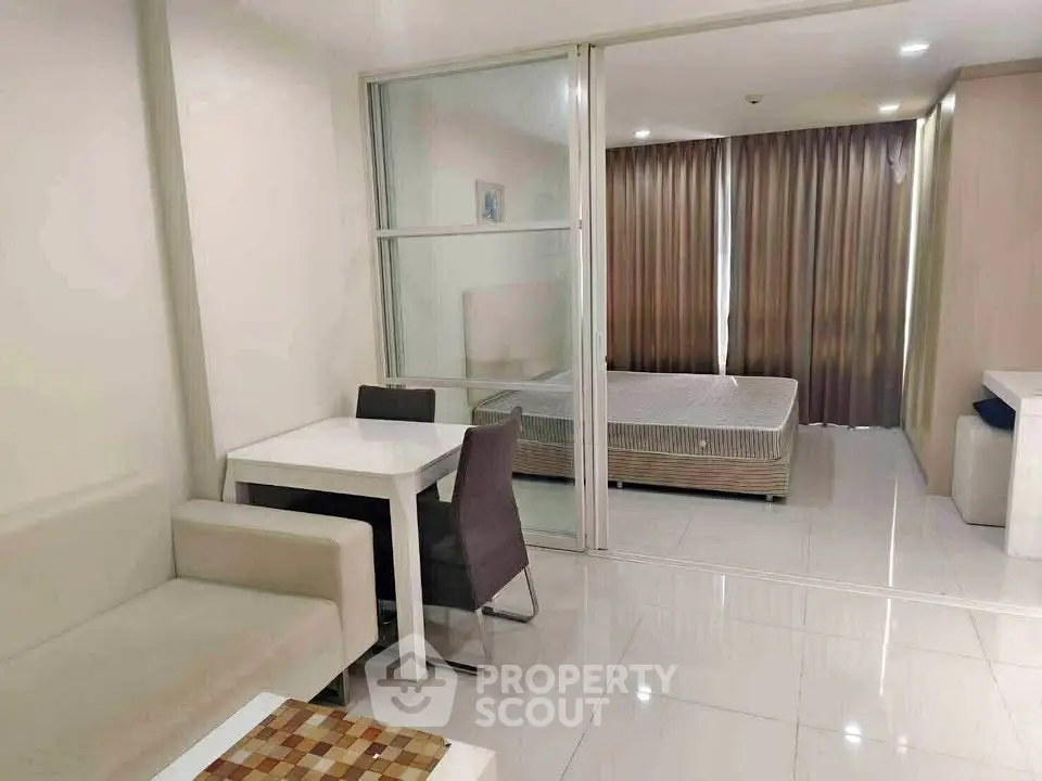 Modern studio apartment with open layout, featuring a cozy living area and bedroom separated by glass partition.
