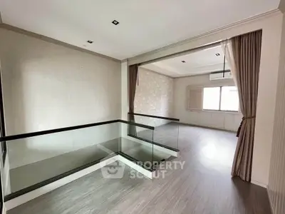 Spacious modern living area with elegant glass railing and large window for natural light.