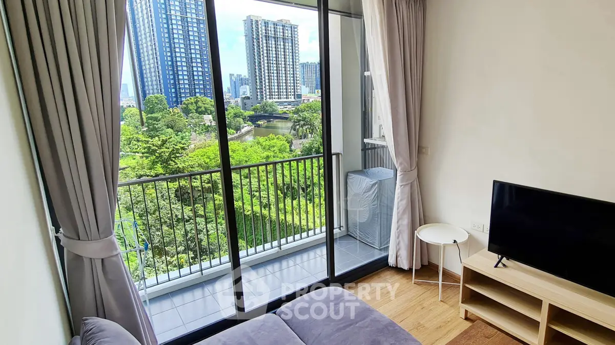 Modern living room with balcony view of cityscape and greenery, featuring sleek furniture and large windows.