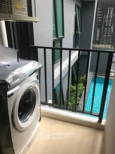Modern balcony with washing machine overlooking pool in urban apartment complex.
