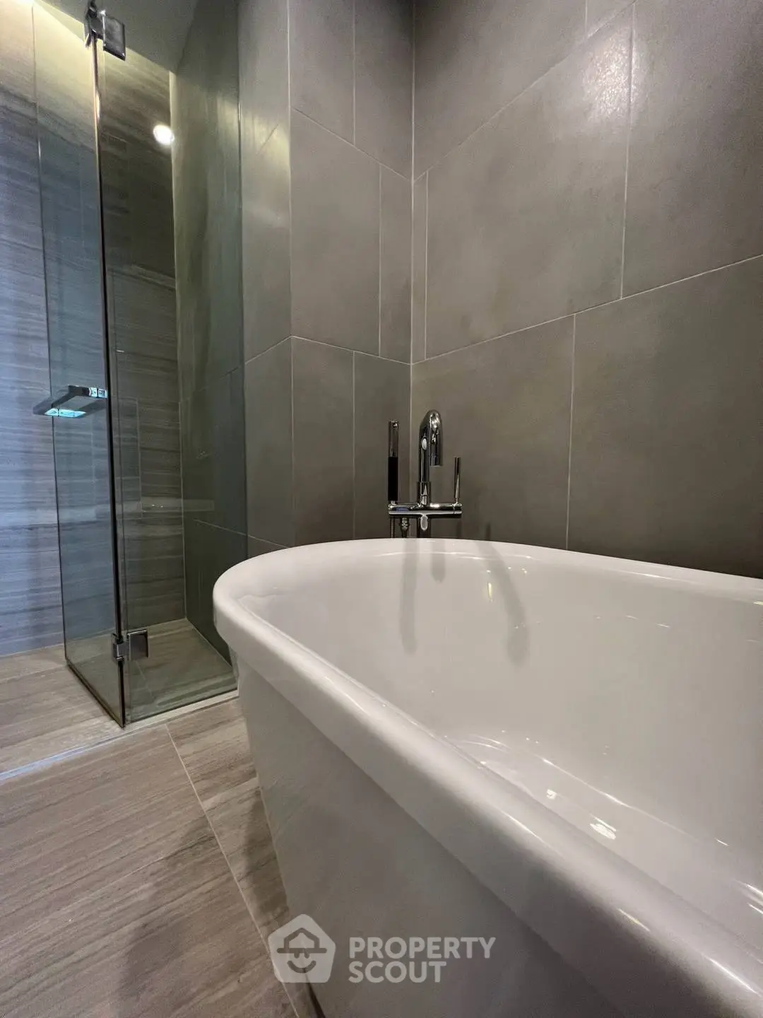 Modern bathroom with sleek bathtub and glass shower enclosure, featuring elegant gray tiles.