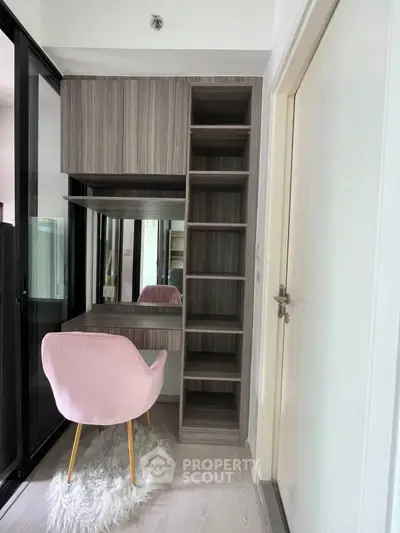 Chic study nook with modern shelving and stylish pink chair in a cozy apartment.