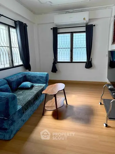 Bright living room with blue sofa and modern decor, featuring large windows and wooden flooring.