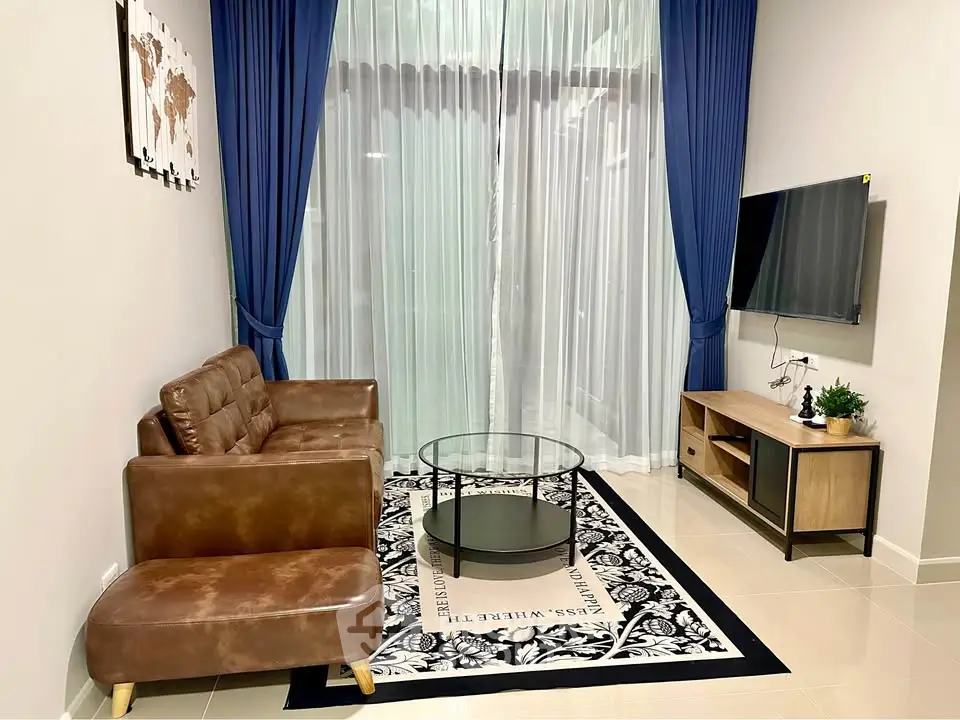 Modern living room with leather sofa, glass coffee table, and wall-mounted TV, featuring elegant blue curtains.