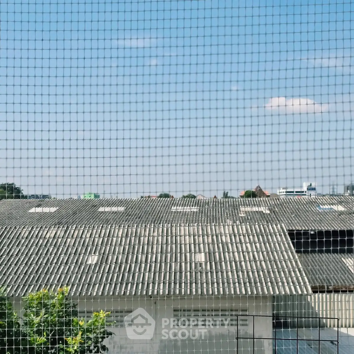 View of industrial building roof through a mesh screen under clear blue sky.