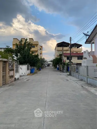 Charming residential street with modern houses and lush greenery under a picturesque sky.