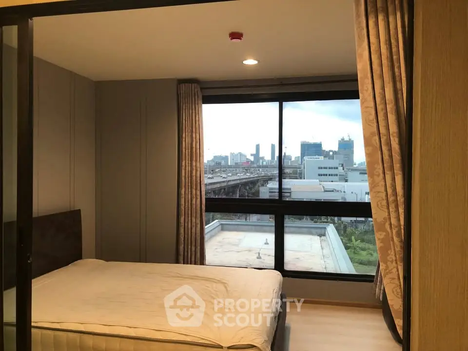 Spacious bedroom with large window offering stunning city view in modern apartment.