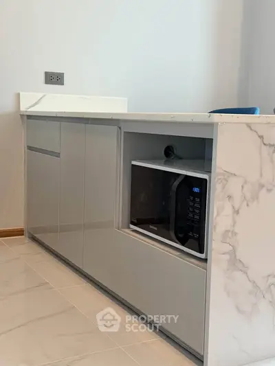 Modern kitchen with sleek cabinetry and built-in microwave, featuring elegant marble countertop.