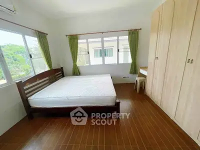 Spacious bedroom with large windows and wooden furniture in a serene setting.