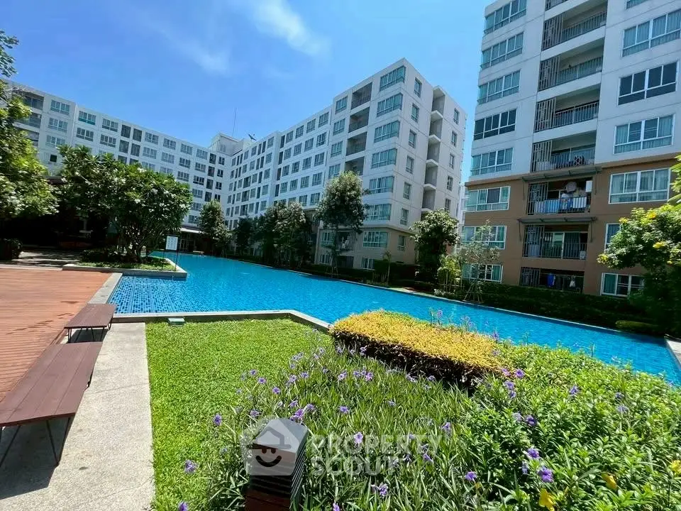 Modern apartment complex with a large swimming pool and lush garden area.