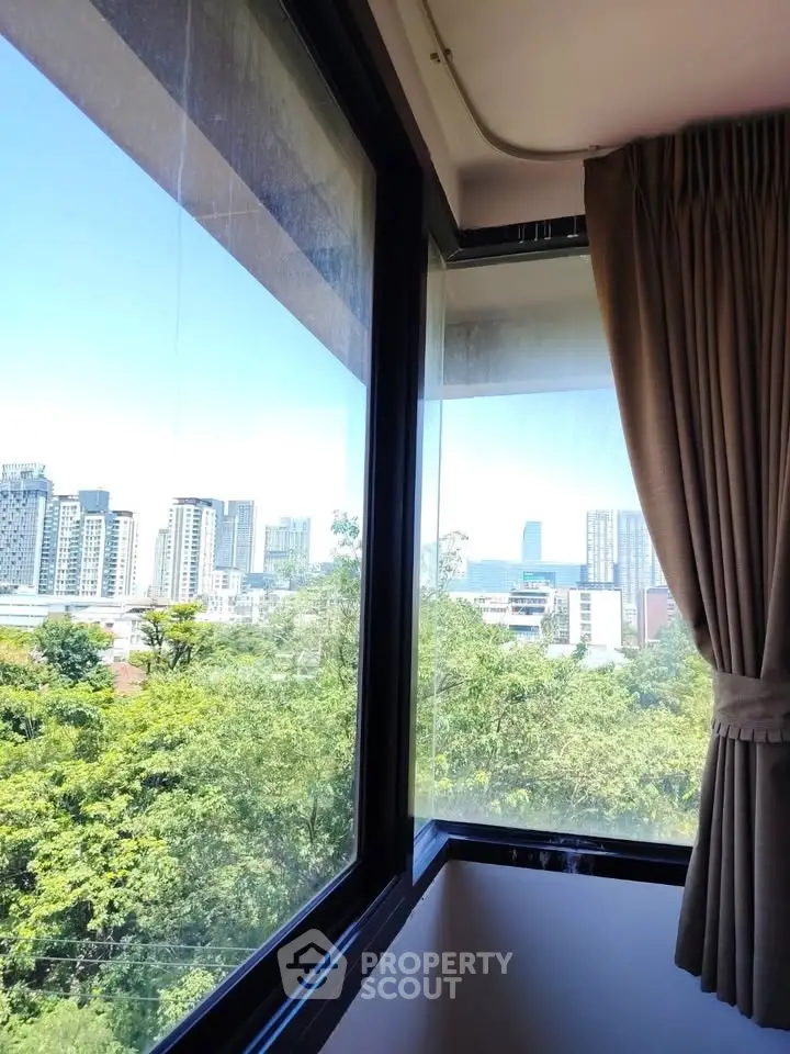 Stunning cityscape view from a high-rise apartment window with lush greenery.