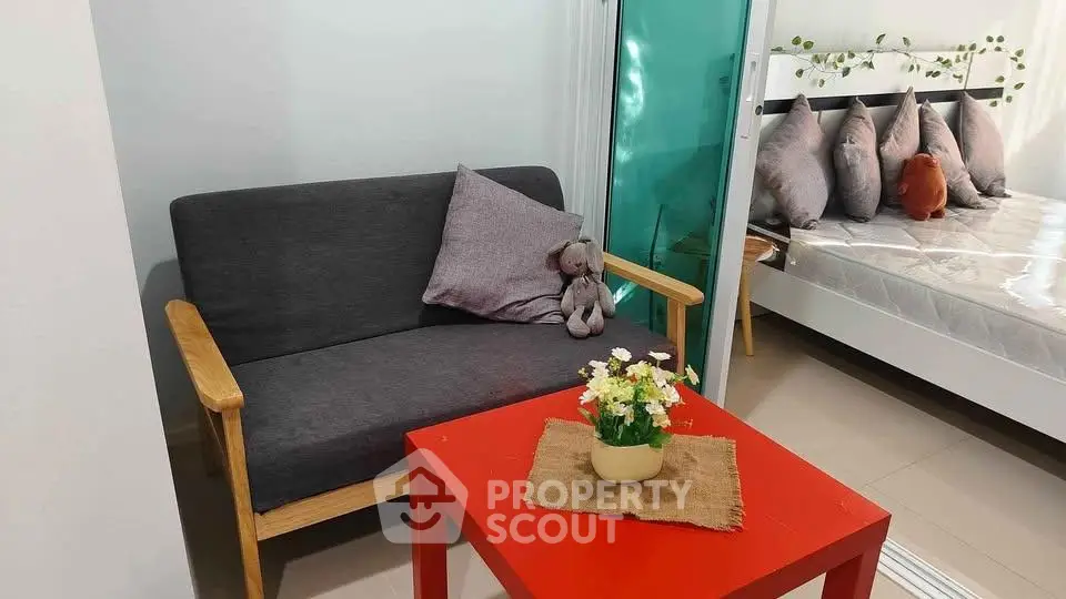 Cozy living area with modern sofa and vibrant red table, adjacent to a stylish bedroom.