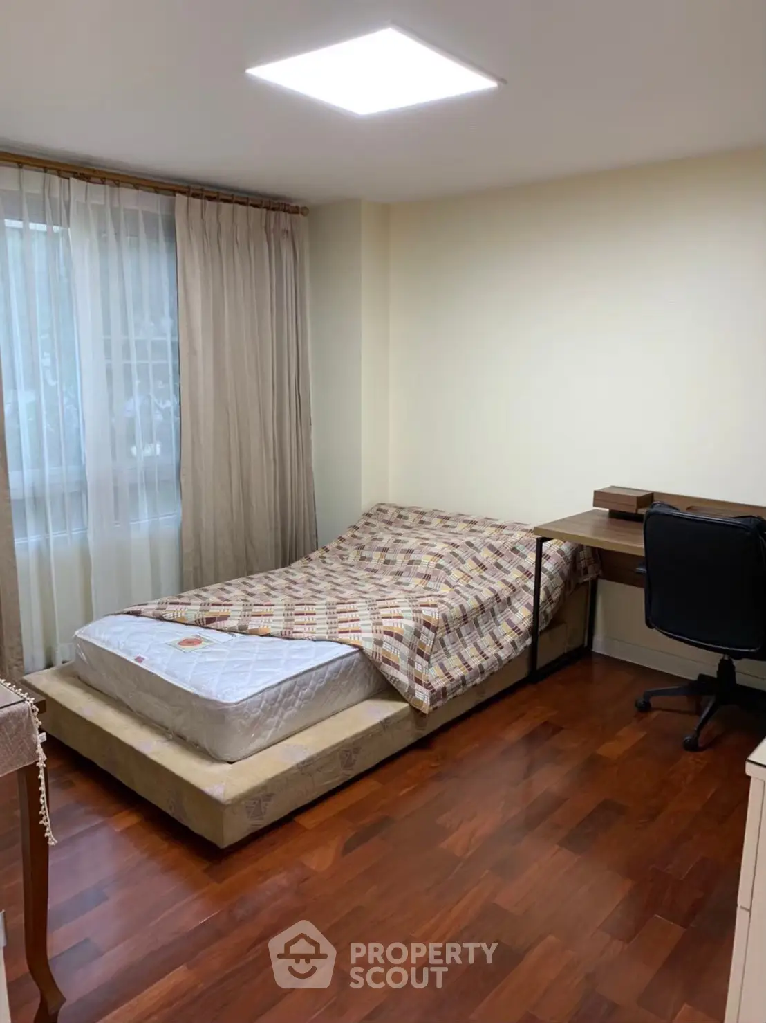 Cozy bedroom with wooden flooring and natural light, featuring a bed and study desk.