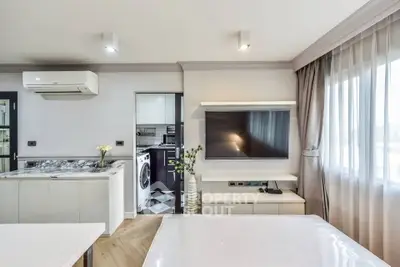 Modern open-plan living room with kitchen and large TV, featuring stylish decor and natural light.