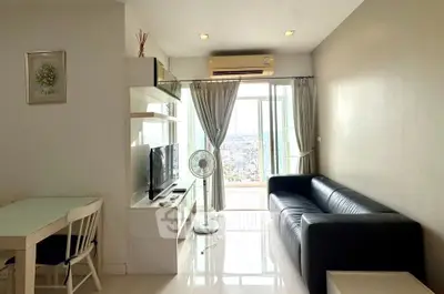 Modern living room with balcony and city view, featuring sleek black sofa and wall-mounted TV.