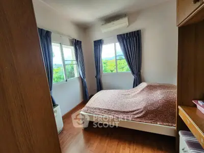 Cozy bedroom with large windows and scenic views, featuring wooden flooring and elegant curtains.