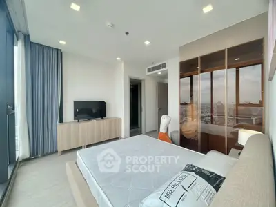 Modern bedroom with large windows and city view, featuring sleek furniture and ample natural light.