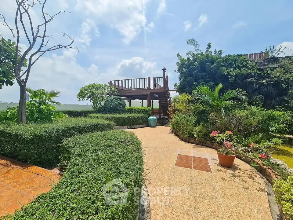 Stunning garden with lush greenery and elevated wooden deck under a bright blue sky.