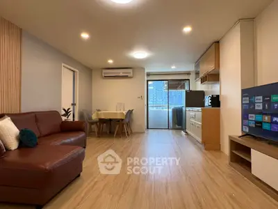 Modern living room with open kitchen and balcony view, featuring sleek furniture and wooden flooring.