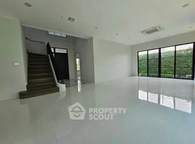 Spacious modern living room with large windows and staircase, perfect for natural light lovers.