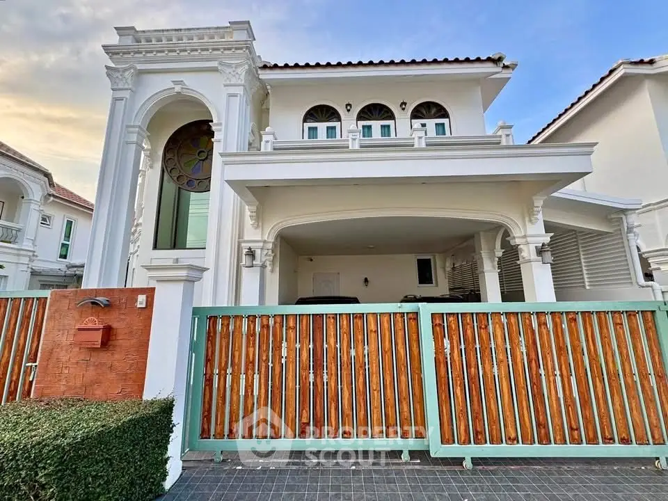 Elegant two-story house with arched windows and wooden gate in a serene neighborhood.