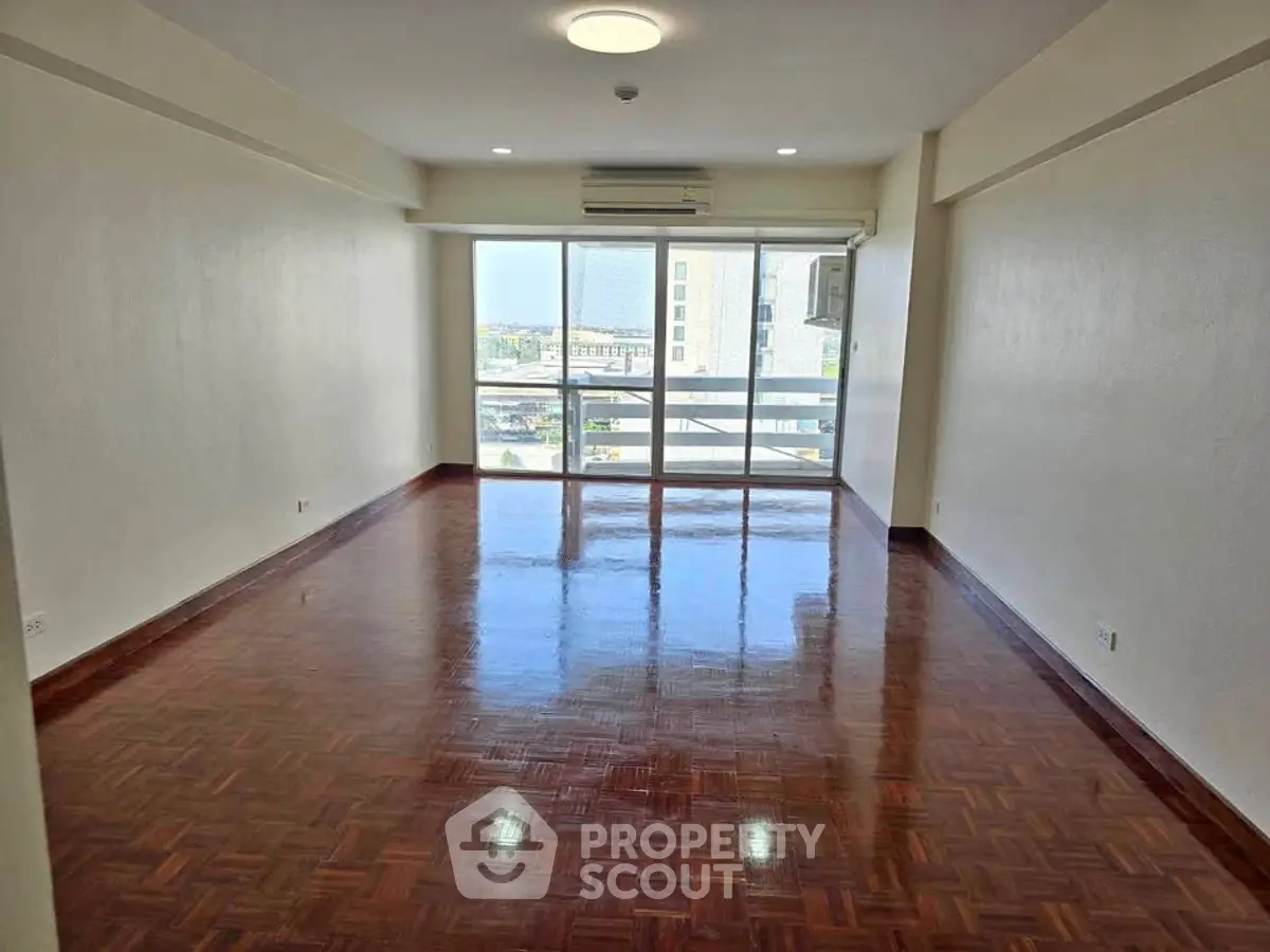 Spacious empty living room with polished wooden floors and large window view.
