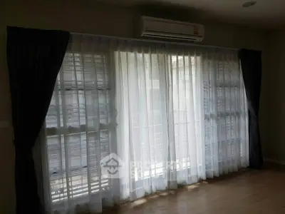 Spacious living room with large windows and elegant curtains, featuring a modern air conditioning unit.